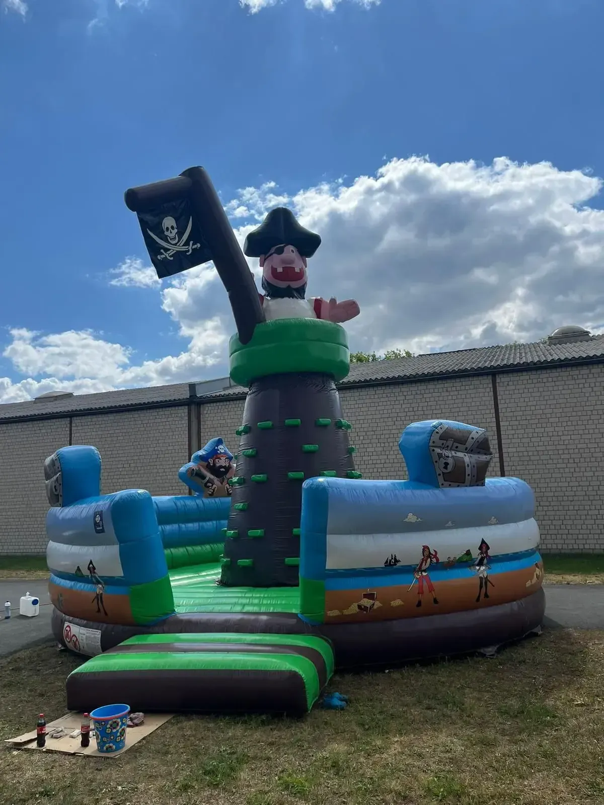 Eine aufblasbare Piratenschiff-Hüpfburg mit zentralem Kletterturm vor blauem, bewölktem Himmel.