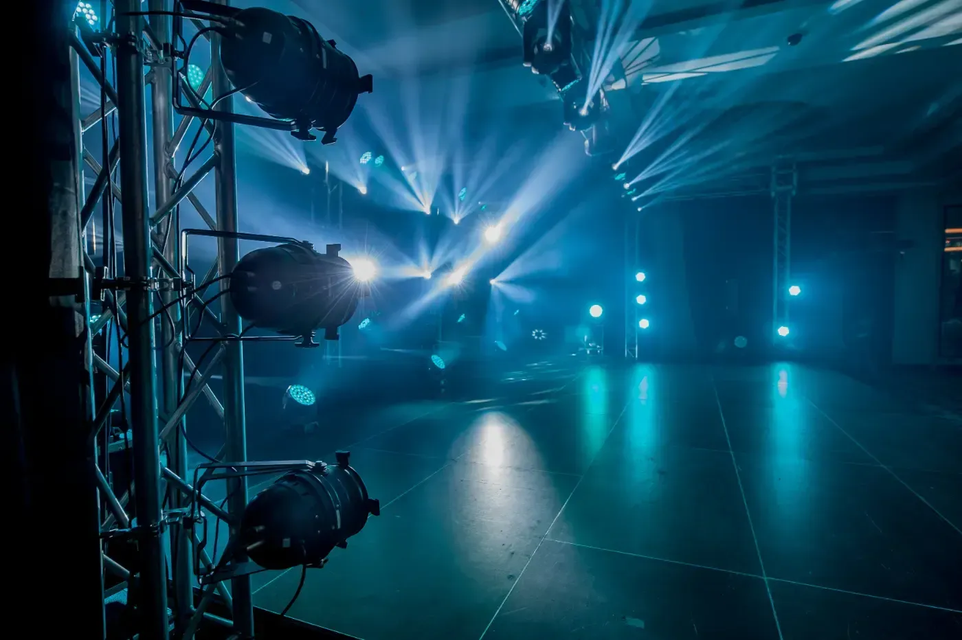 Eine Bühnenbeleuchtungsanlage mit hellblauen Scheinwerfern, die auf eine leere Bühne in einem dunklen Veranstaltungsort strahlen.