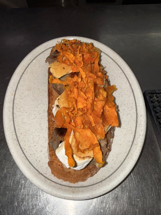 Taco cubierto con relleno de naranja rallado sobre un plato blanco moteado, en una mesa oscura.