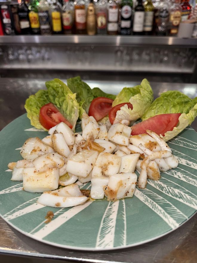 Plato de vieiras selladas con guarnición de lechuga y tomate en una barra.