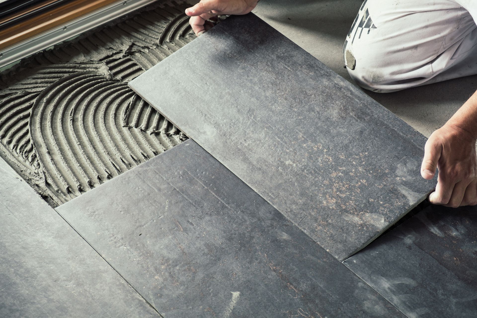 Un ouvrier pose des carreaux de céramique gris foncé sur une surface adhésive