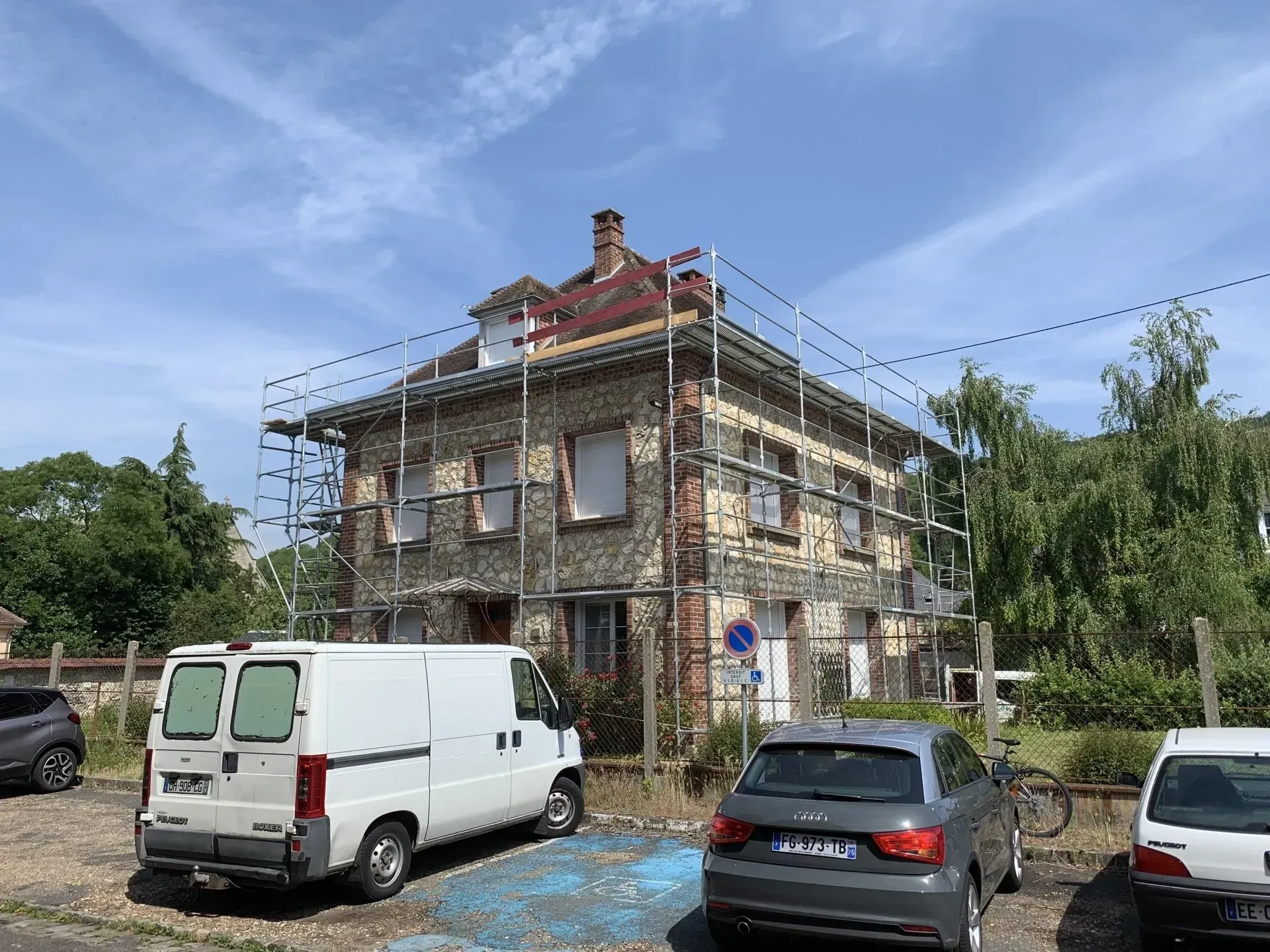 Plusieurs véhicules garés devant une maison avec échafaudages