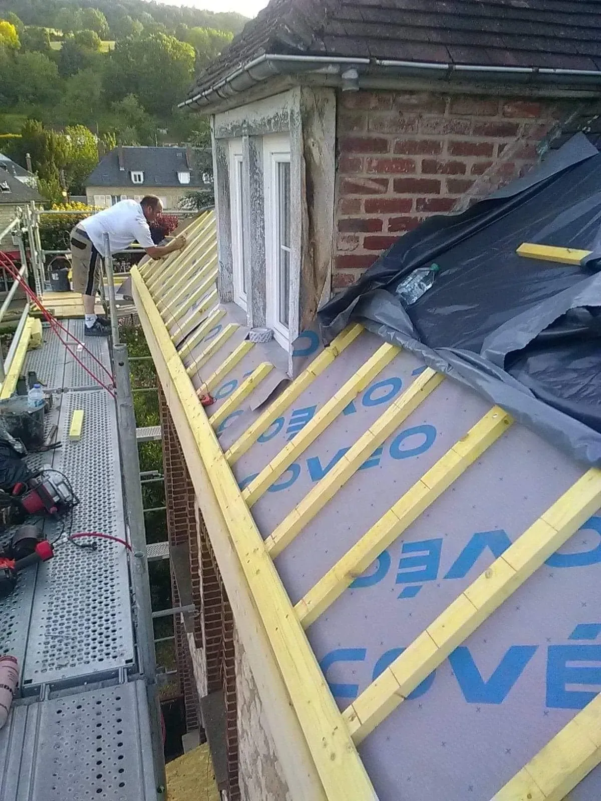 Un artisan sur un échafaudage travaillant sur la charpente d'une maison