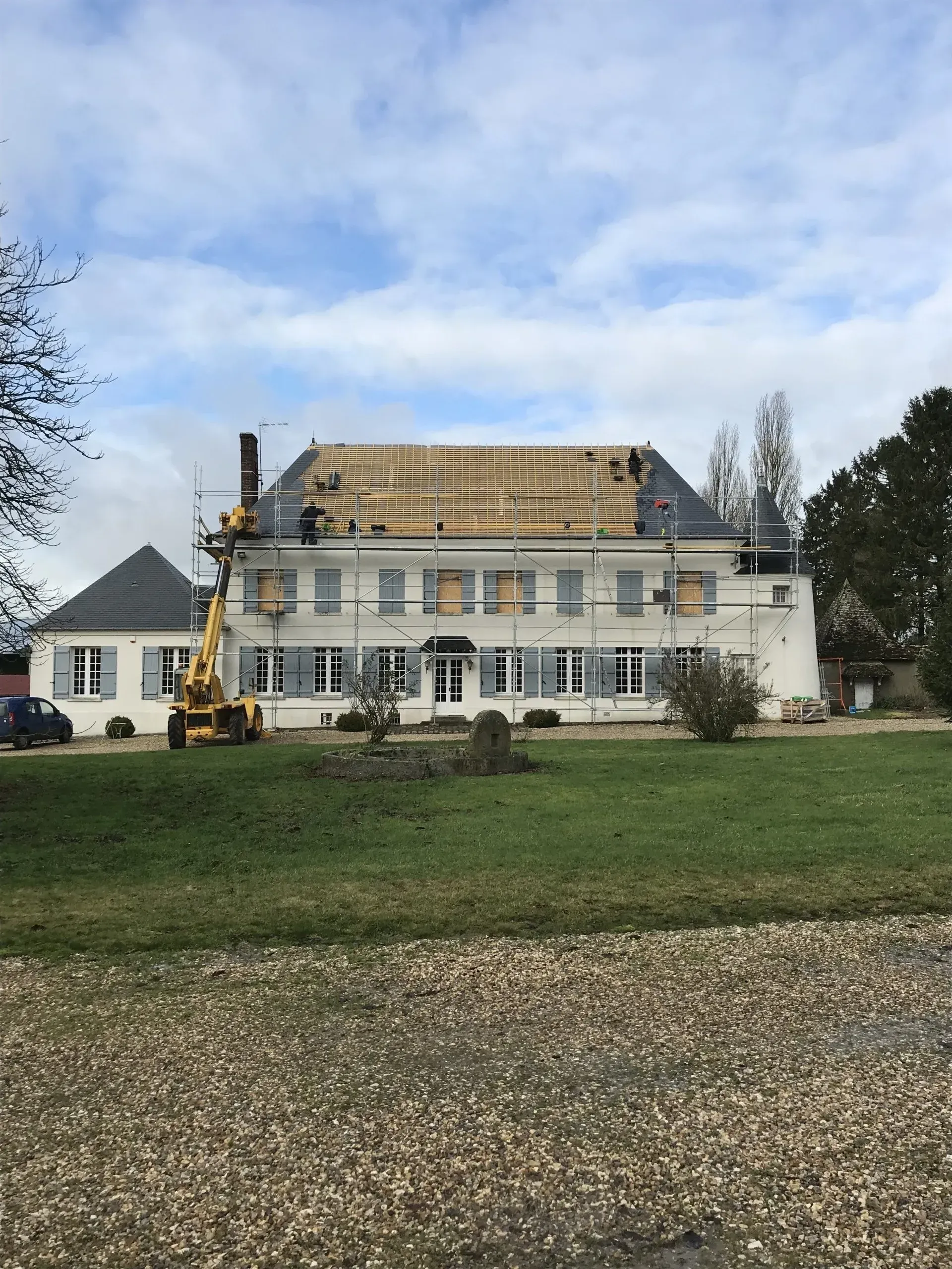 Grande habitation où les artisans sont en train de poser des plaques d'ardoise pour la toiture