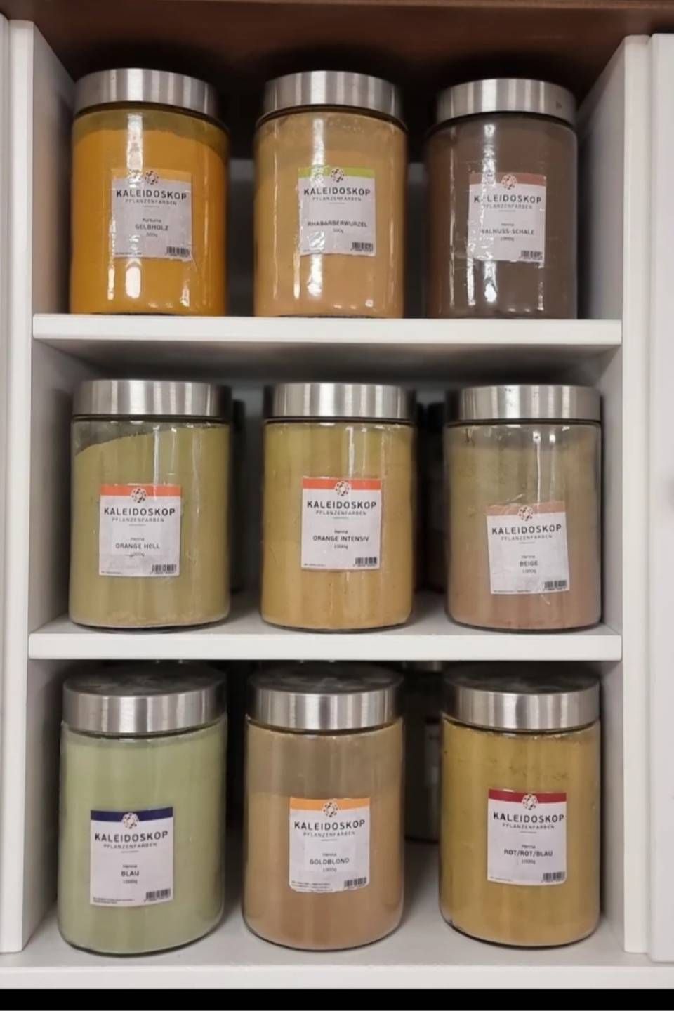 Gewürzgläser in einem weissen Schrank, ordentlich auf Regalen angeordnet. Gläser mit Gewürzen in verschiedenen Farben.