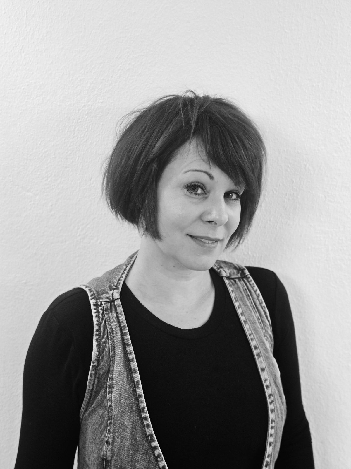 Eine Frau in Jeansweste und schwarzem Hemd lächelt und blickt in die Kamera.