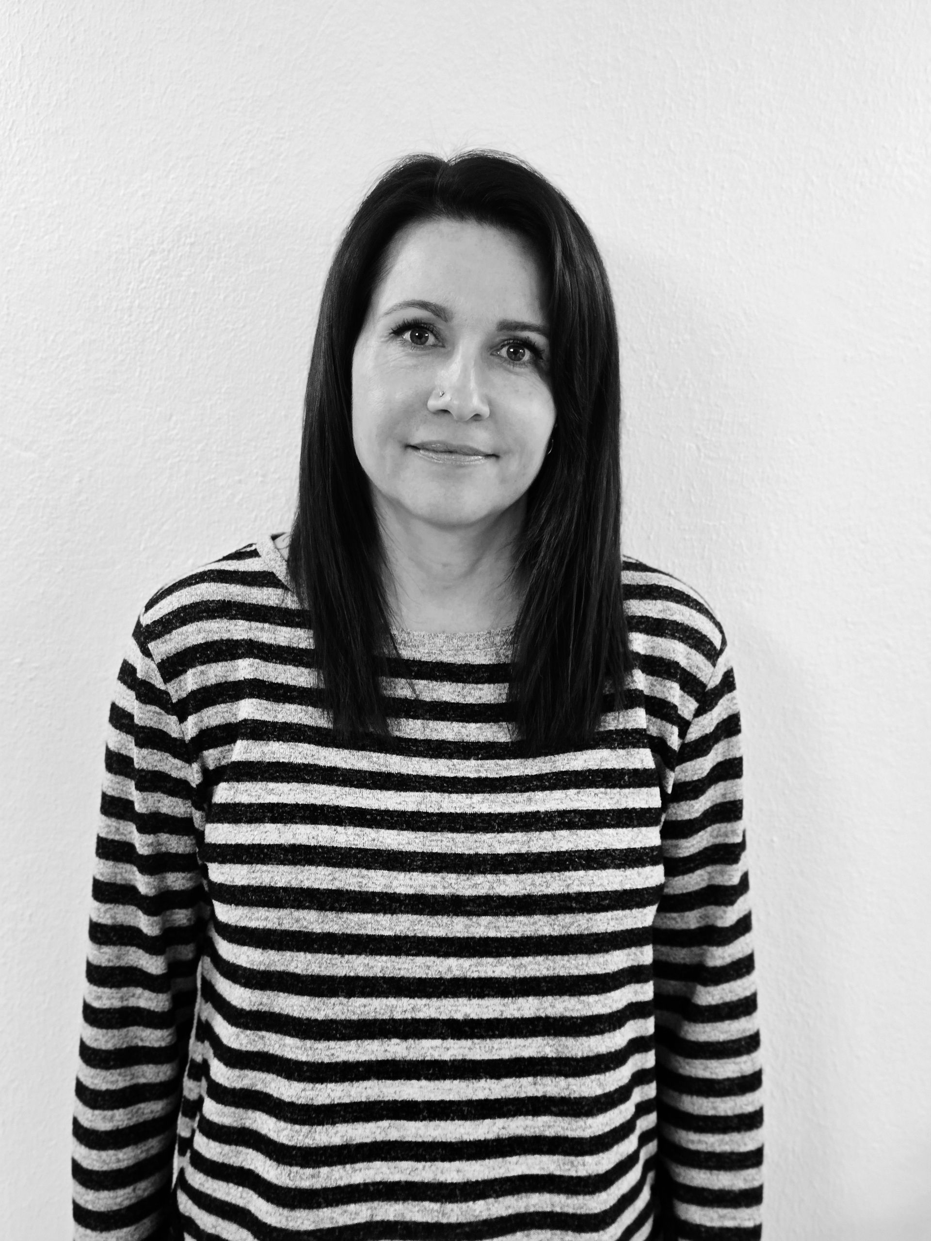 Frau mit dunklen Haaren, die einen gestreiften Pullover trägt, steht vor einer schlichten Wand.