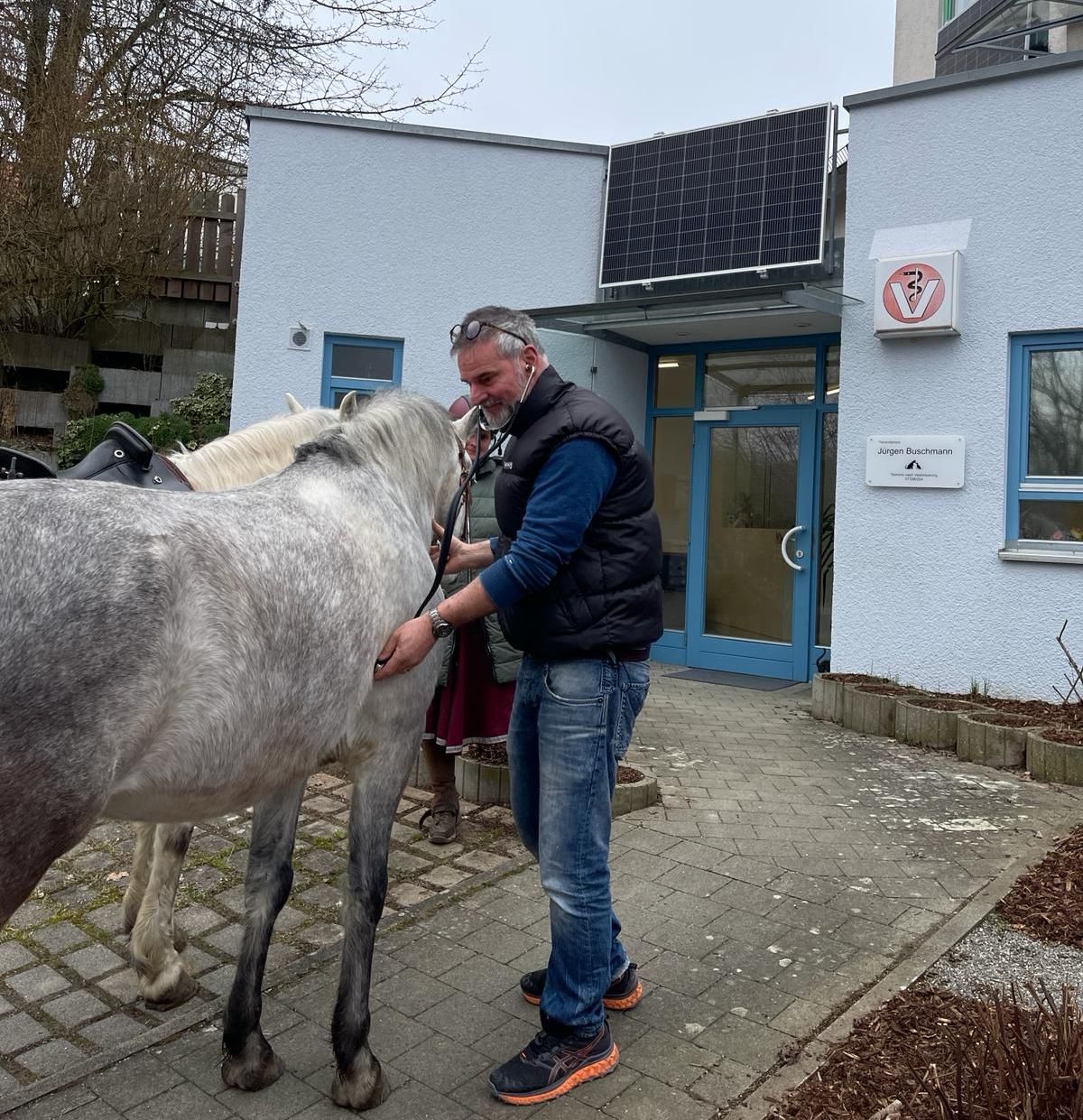 Ein Mann steht neben einem Pferd vor einem Gebäude | Tierarztpraxis Buschmann