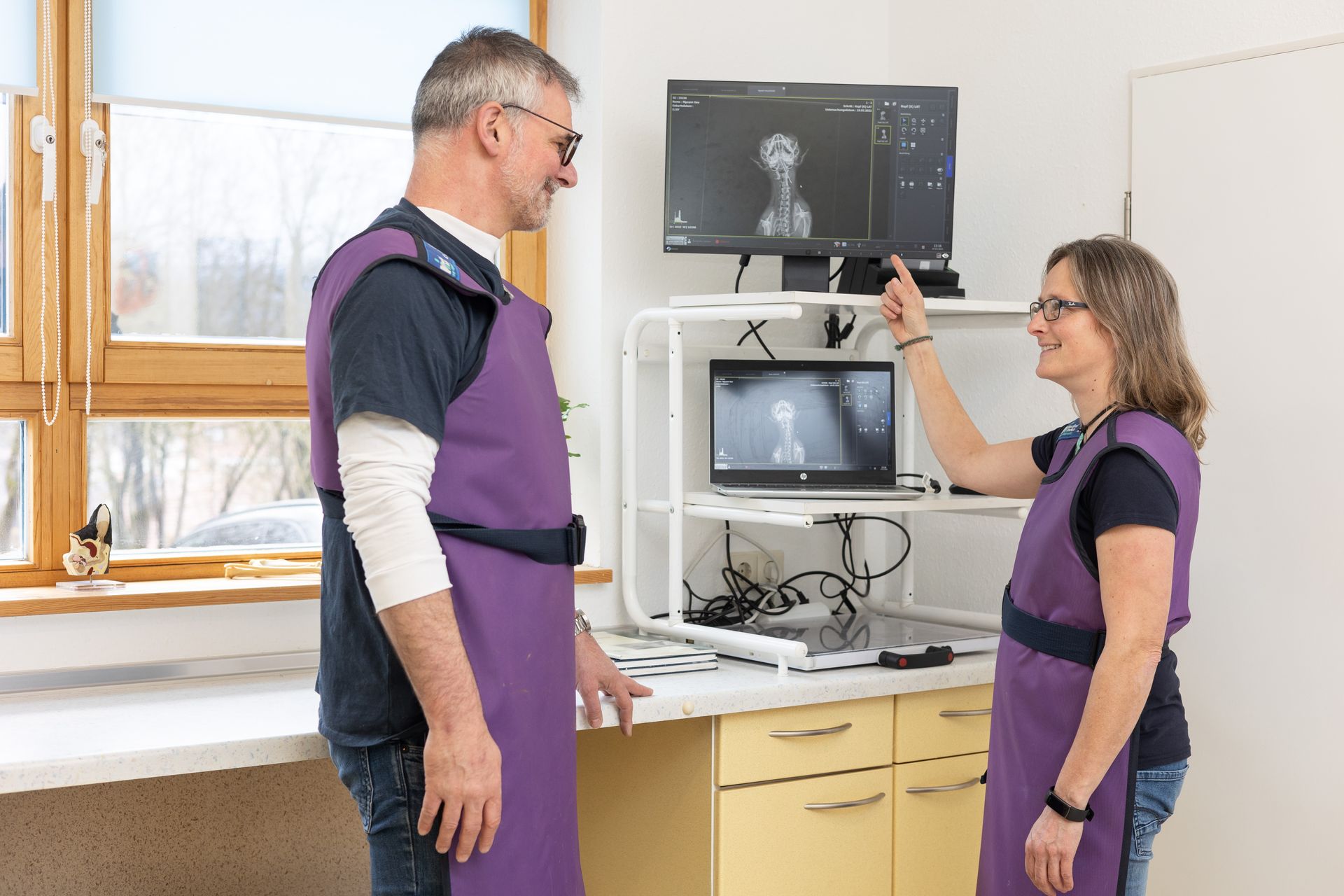 Zwei Personen mit lila Schürzen schauen in einer medizinischen Umgebung auf einen Computerbildschirm.