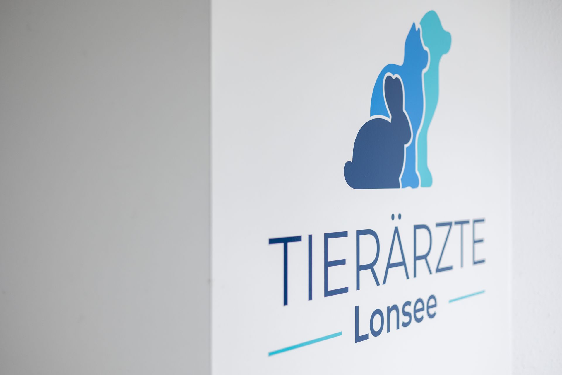 Schild der Tierärzte Lonsee mit den Silhouetten von Hund, Katze und Kaninchen in Blautönen.