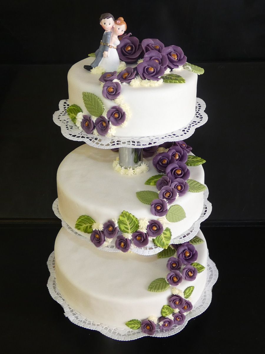 Dreistöckige weiße Hochzeitstorte mit lila Rosen und einer Brautpaarfigur als Tortenfigur