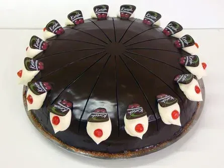 Schokoladenkuchen mit weißen Sahnehäubchen und kreisförmig angeordneten Kirschen.