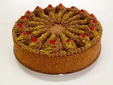 Runder Kuchen mit braunen Krümeln an den Seiten und aufgespritzten grünen Zuckergusswirbeln, garniert mit roten Kirschen