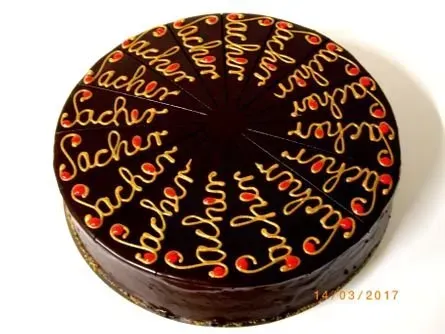 Runder Schokoladenkuchen mit glänzender Ganache und rot-orangefarbenem Schriftzug „Sachertorte“ obenauf