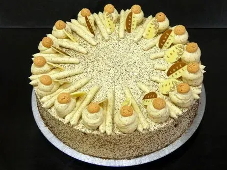 Runder Kuchen mit Sahnetupfen, Waffelröllchen und Nüssen auf einer weißen Platte