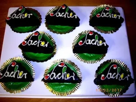 Sieben grün und schwarz verzierte Kuchen auf einem Tablett, jeder mit weißer Schreibschrift