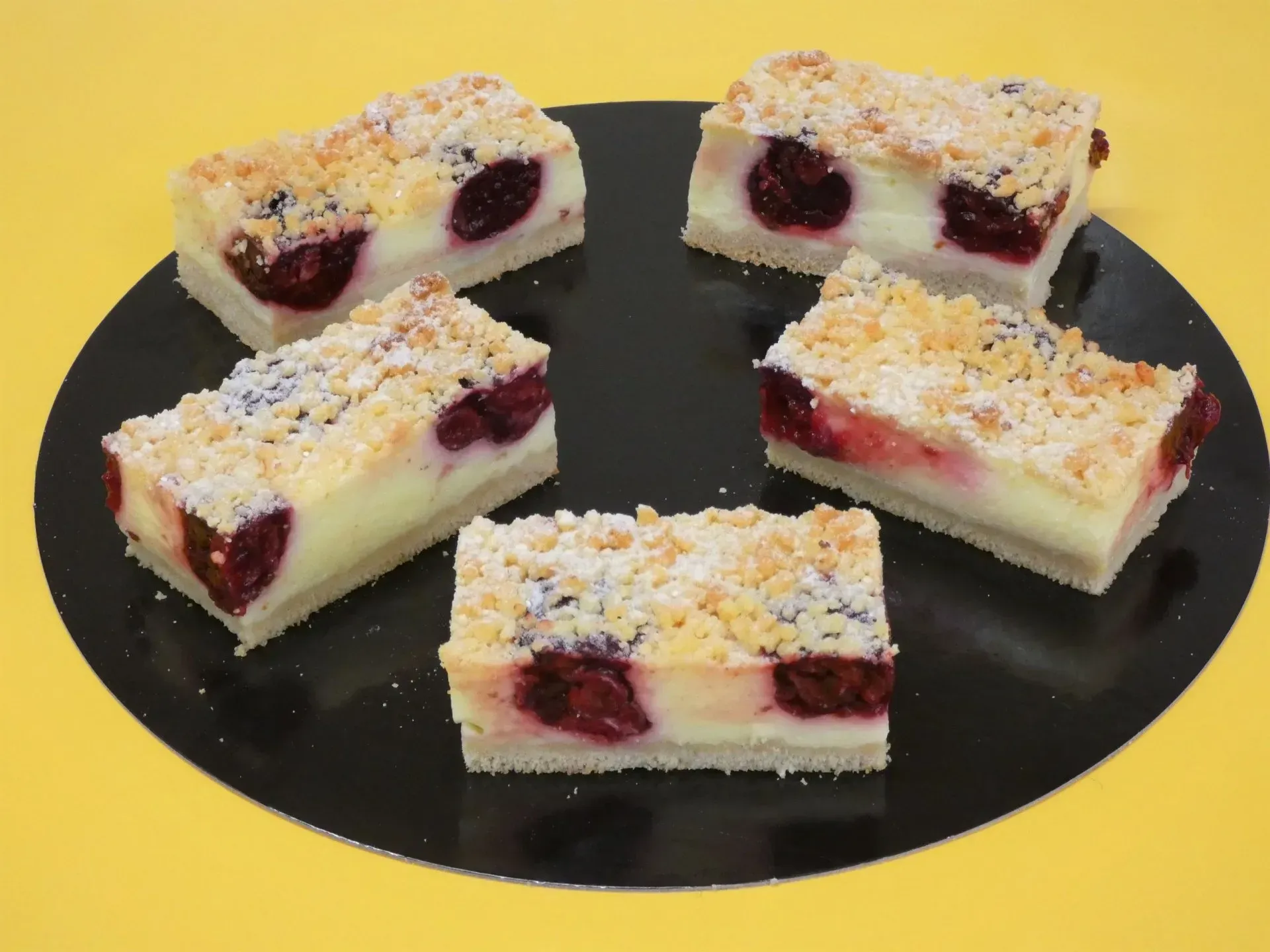 Ein Teller mit vier mit Beeren gefüllten Kuchenriegeln, mit Puderzucker bestäubt, auf einem schwarzen Teller
