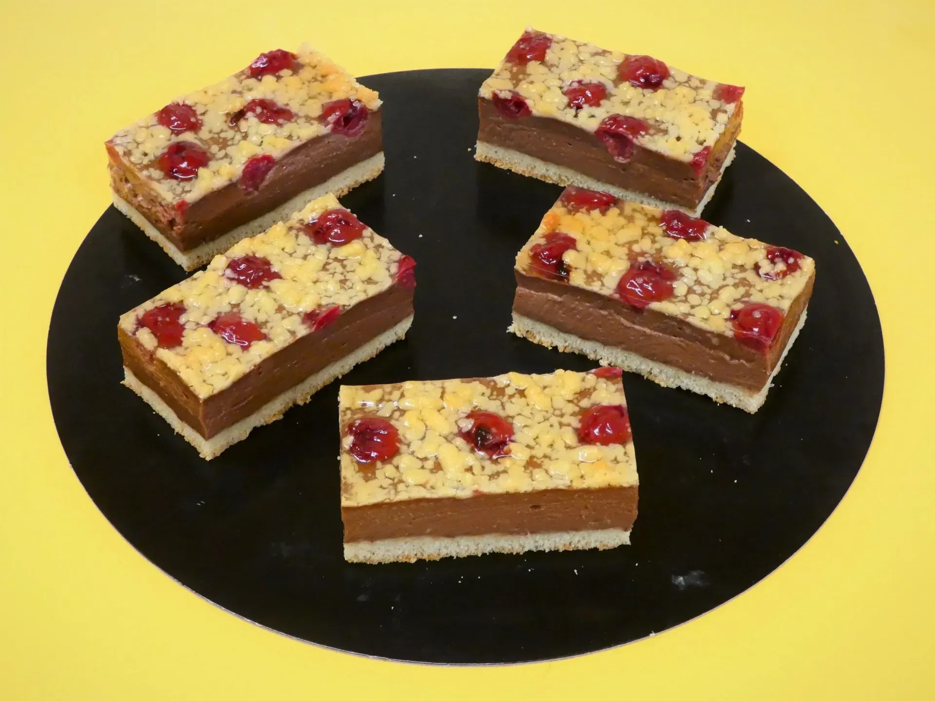 Vier mit Beeren garnierte Dessertquadrate auf einem schwarzen Teller