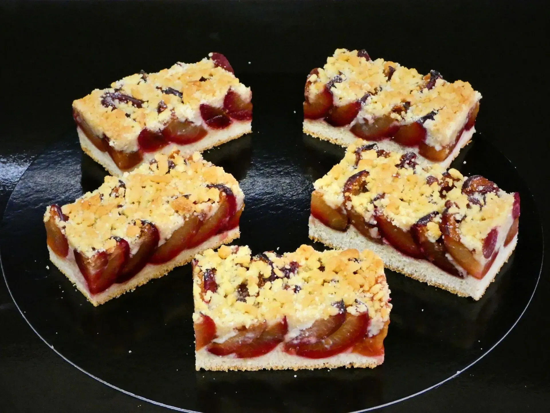Fünf mit Beeren belegte Dessertriegel auf einem dunklen Teller