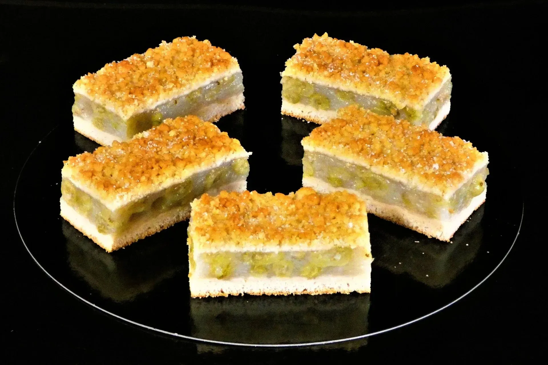 Vier mit goldenen Streuseln überzogene Dessertriegel, angerichtet auf einem schwarzen Teller vor dunklem Hintergrund