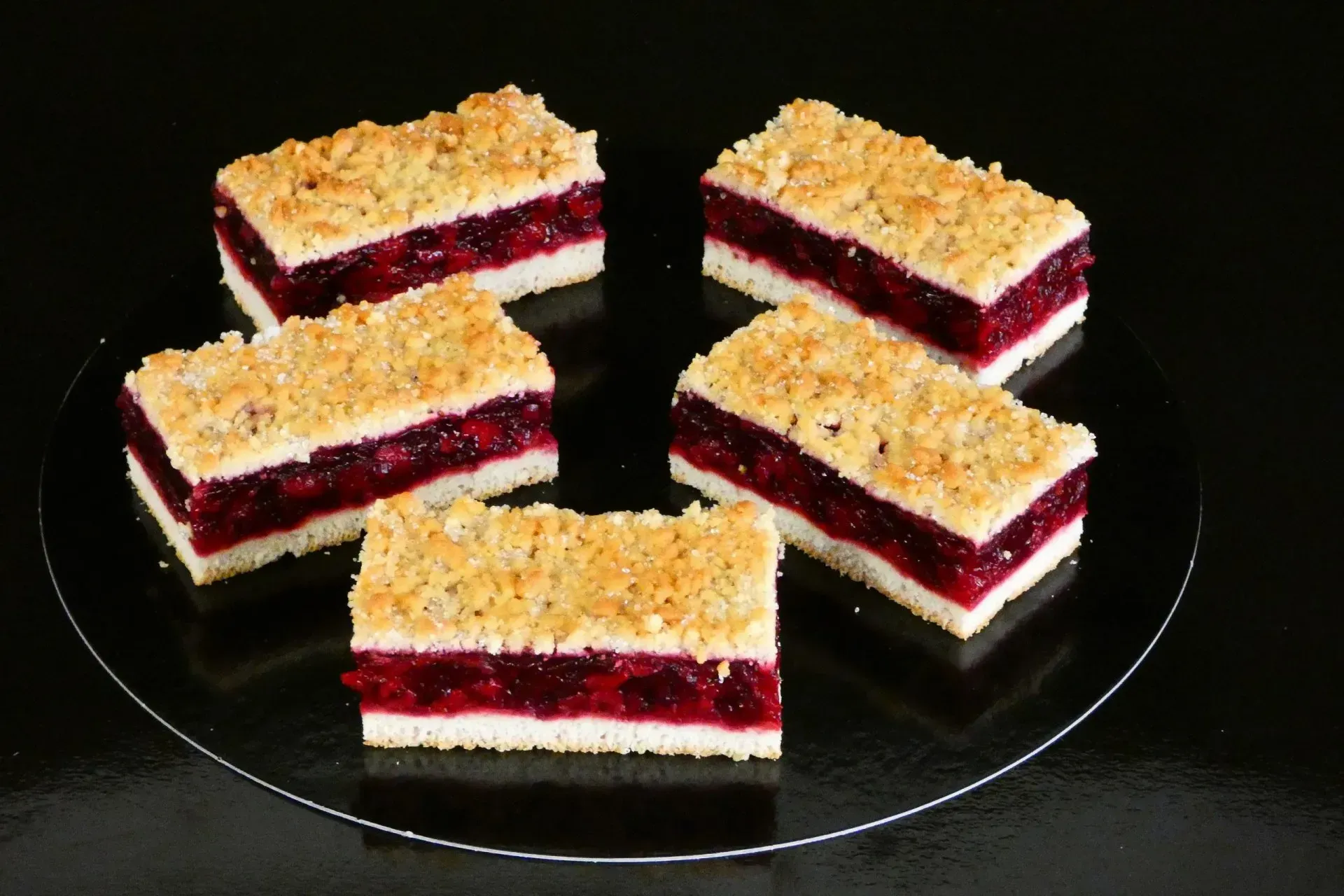 Dessertquadrate mit roter Beerenfüllung und Streuseln auf einem schwarzen Teller