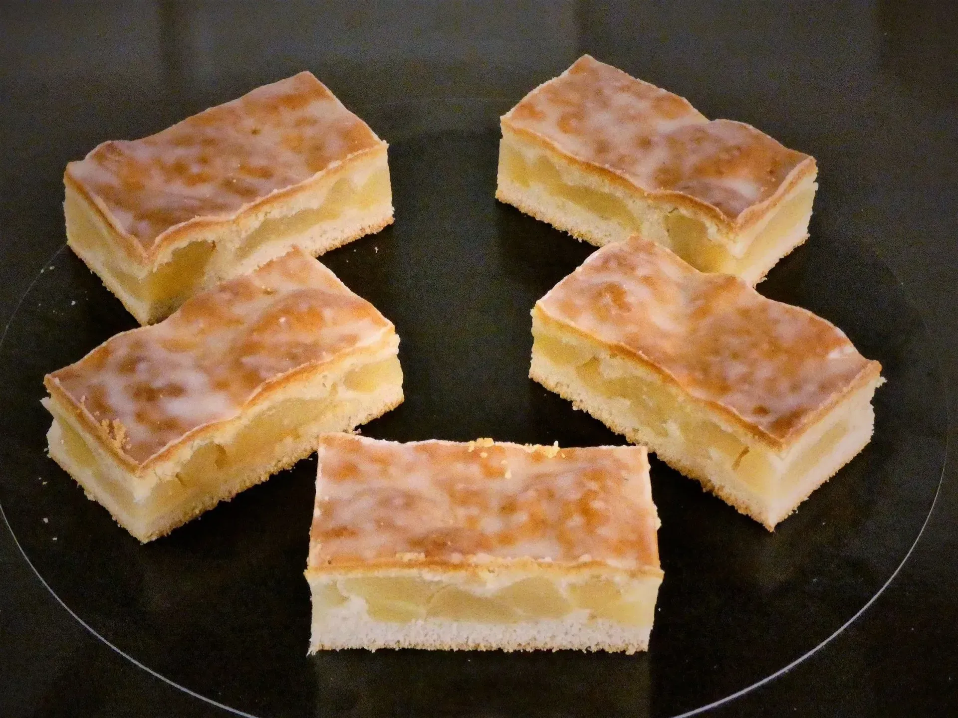 Fünf kleine, quadratische Gebäckstücke mit goldbrauner Oberfläche auf einem dunklen Teller angerichtet.