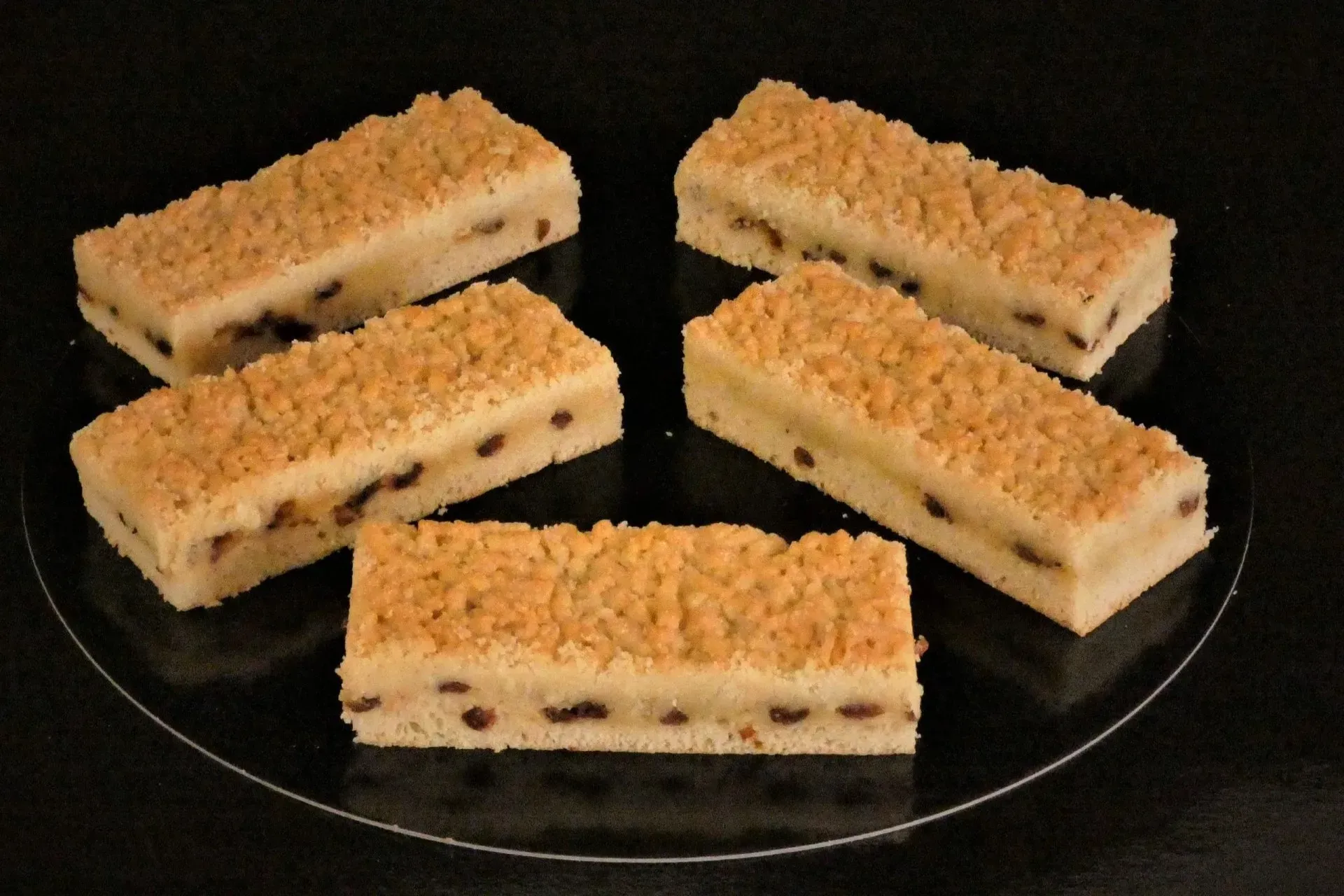 Fünf rechteckige Dessertriegel mit Streuseln auf einer durchsichtigen Glasplatte vor schwarzem Hintergrund