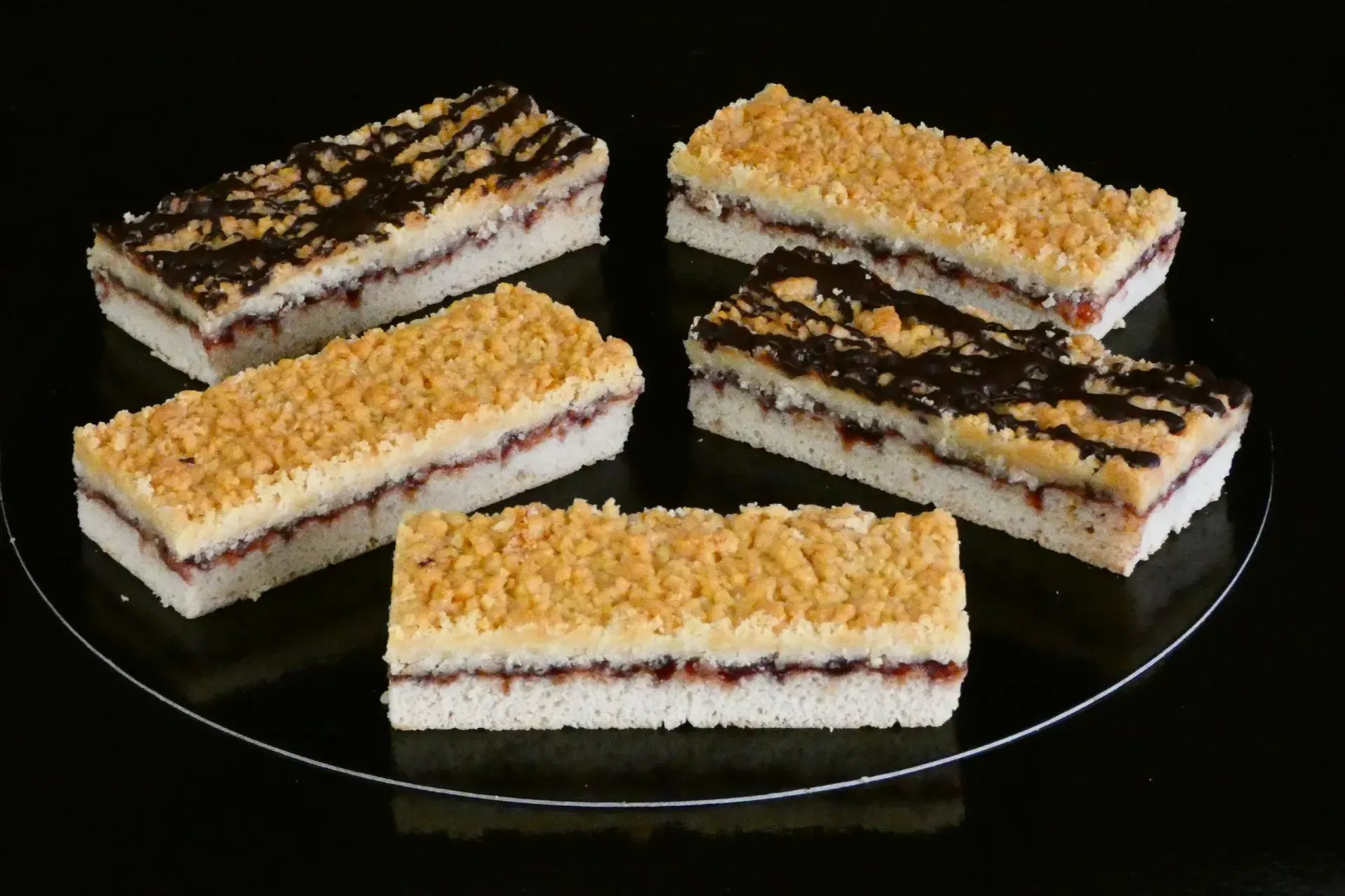 Fünf geschichtete Dessertriegel auf einem Glasteller, bestreut mit gelben und Schokoladenstreuseln.