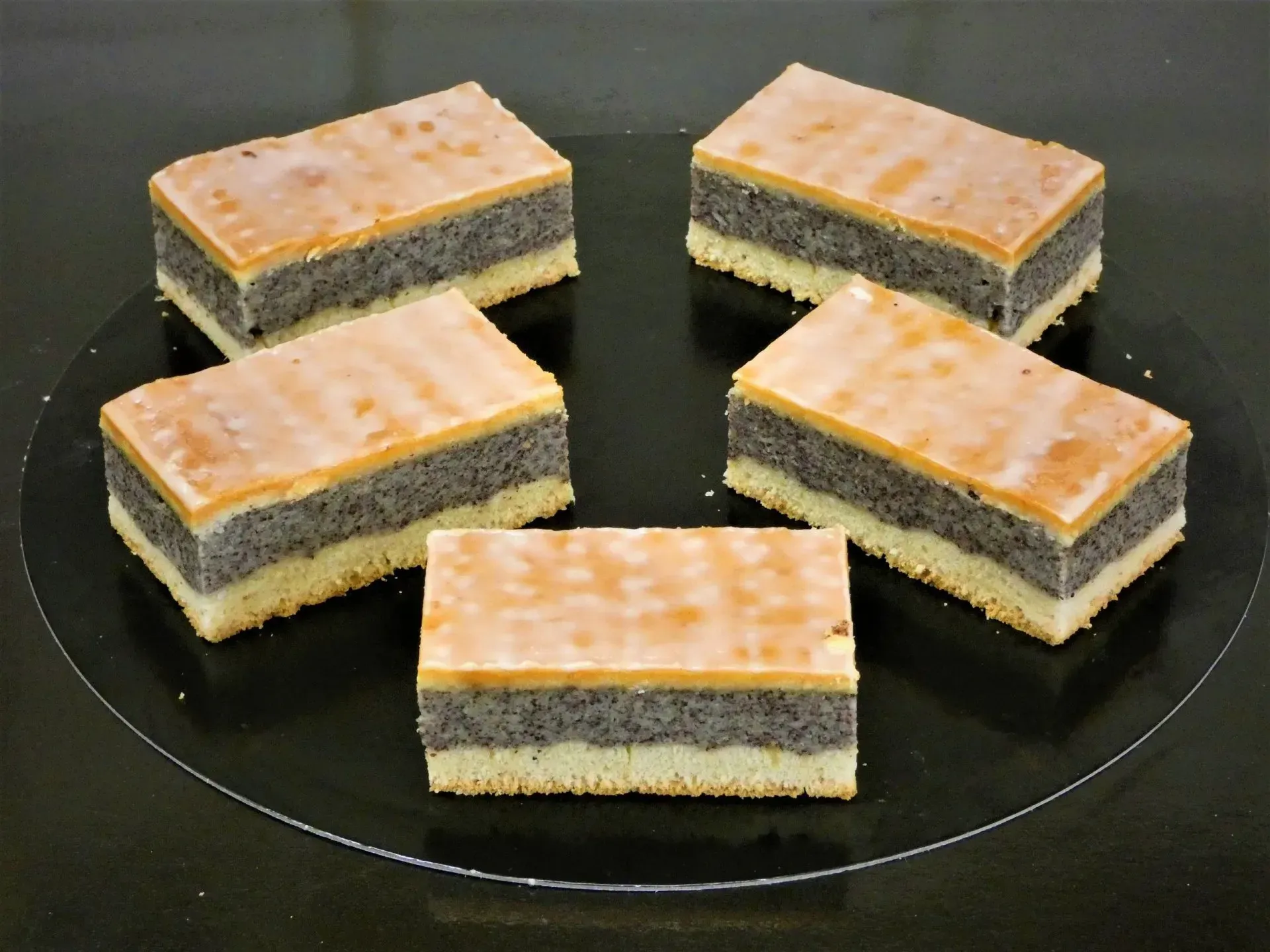 Fünf rechteckige, geschichtete Dessertriegel auf einem schwarzen Teller.