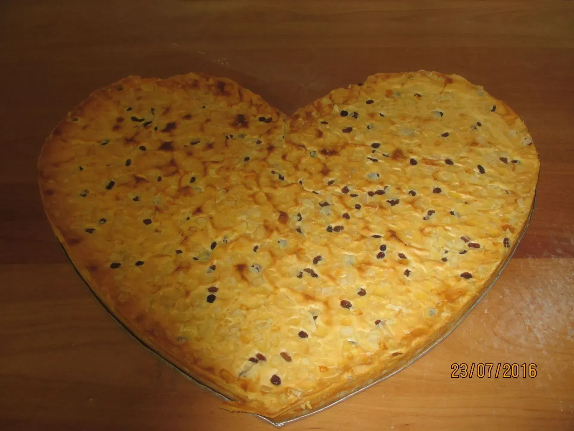 Herzförmiger, goldener Kuchen mit Schokoladenstückchen auf einem Holzsockel