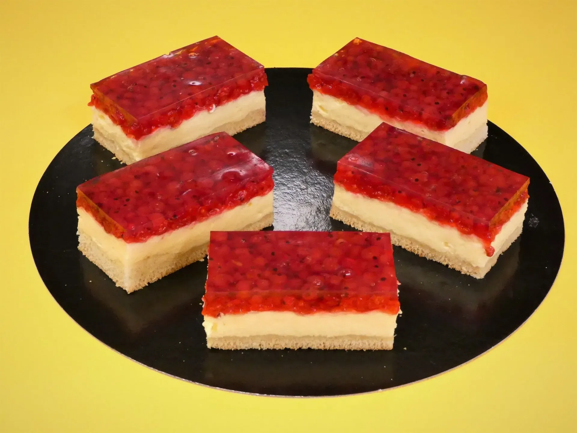 Fünf mit Erdbeeren belegte Dessertquadrate auf einem schwarzen Teller angerichtet.