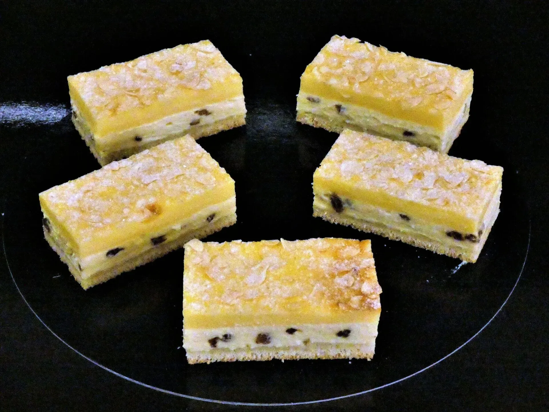Fünf quadratische, geschichtete Dessertriegel, mit Puderzucker bestreut, auf einem schwarzen Teller