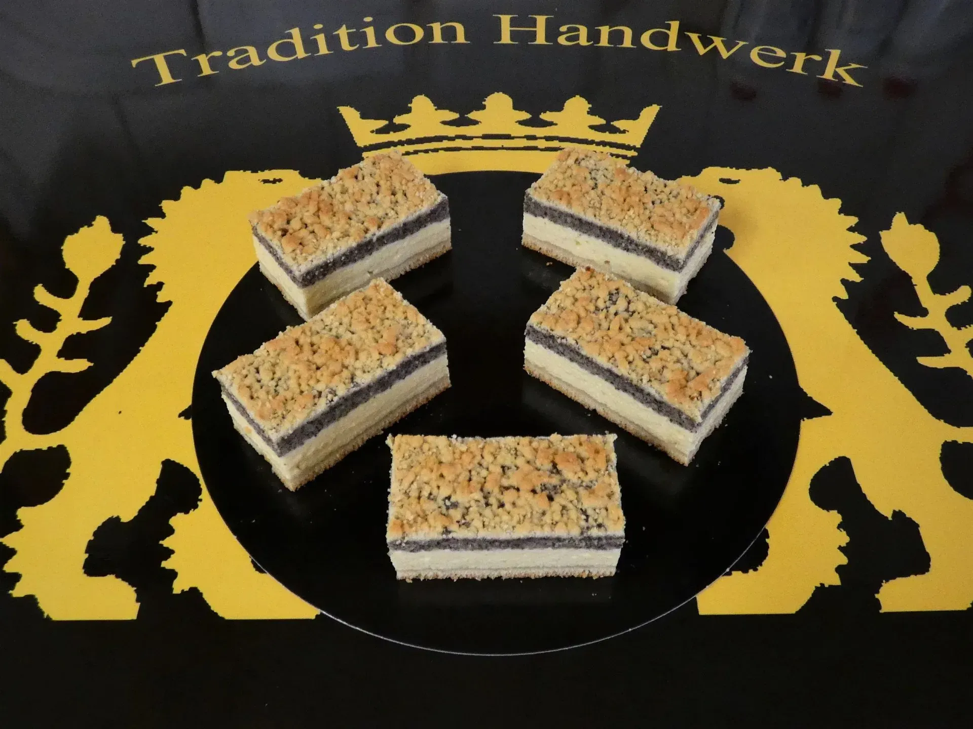 Fünf geschichtete Dessertquadrate mit goldener Glasur neben Tradition Handwerk Schriftzug