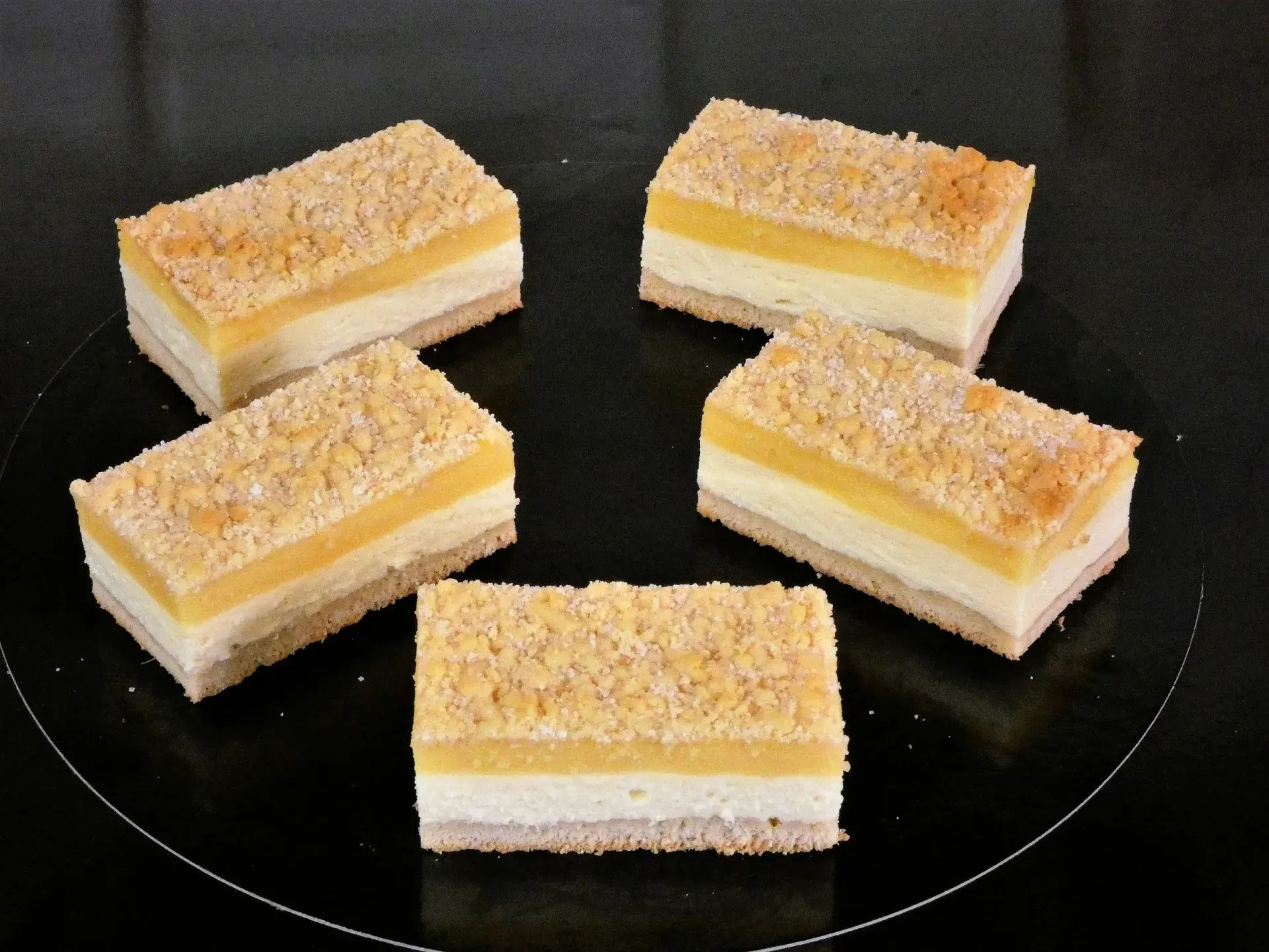Fünf kleine, geschichtete Dessertquadrate mit Puderzucker auf einem dunklen Teller