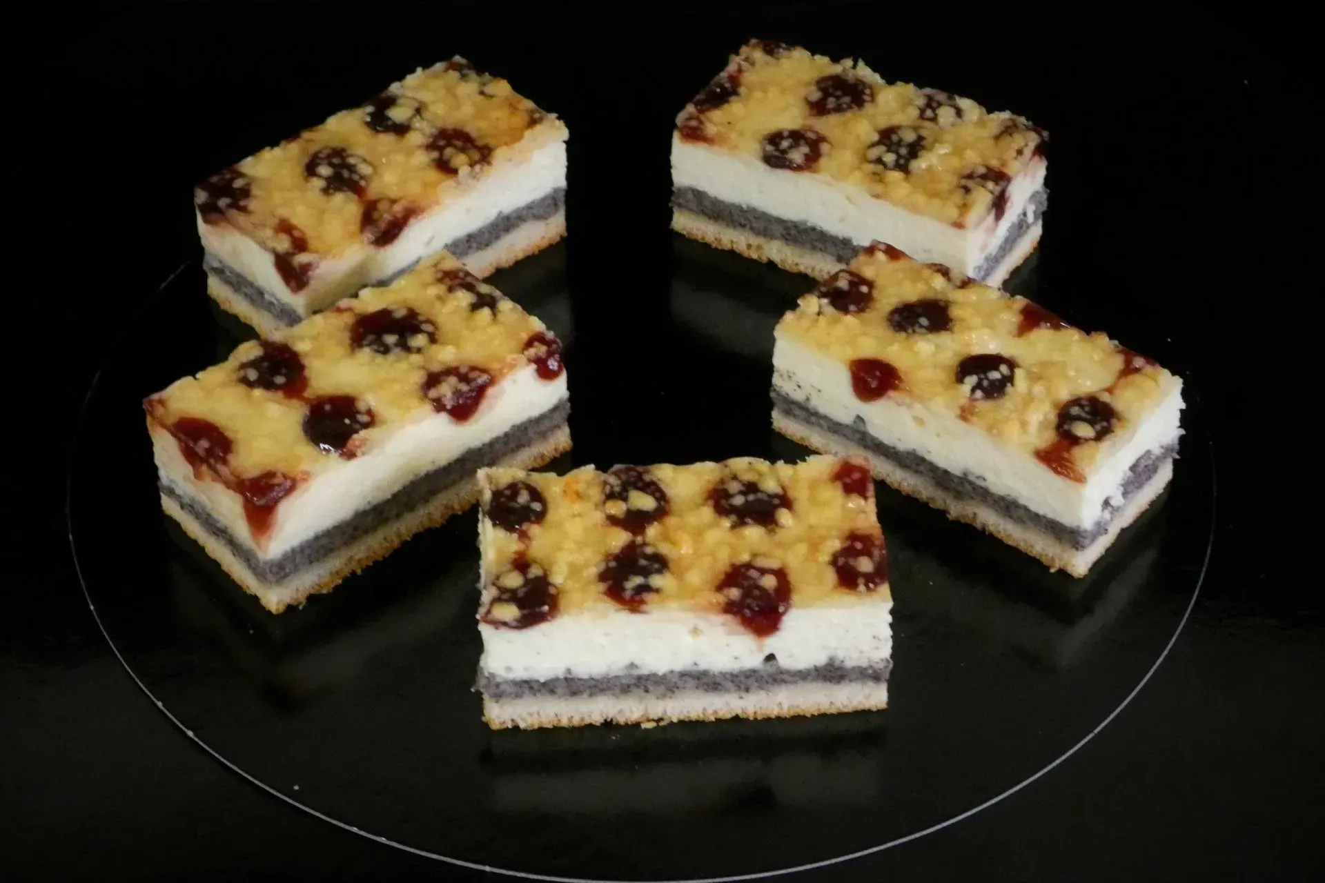 Fünf Stücke geschichteter Sahne- und Früchtekuchen auf einem dunklen Teller, garniert mit Kirschen.