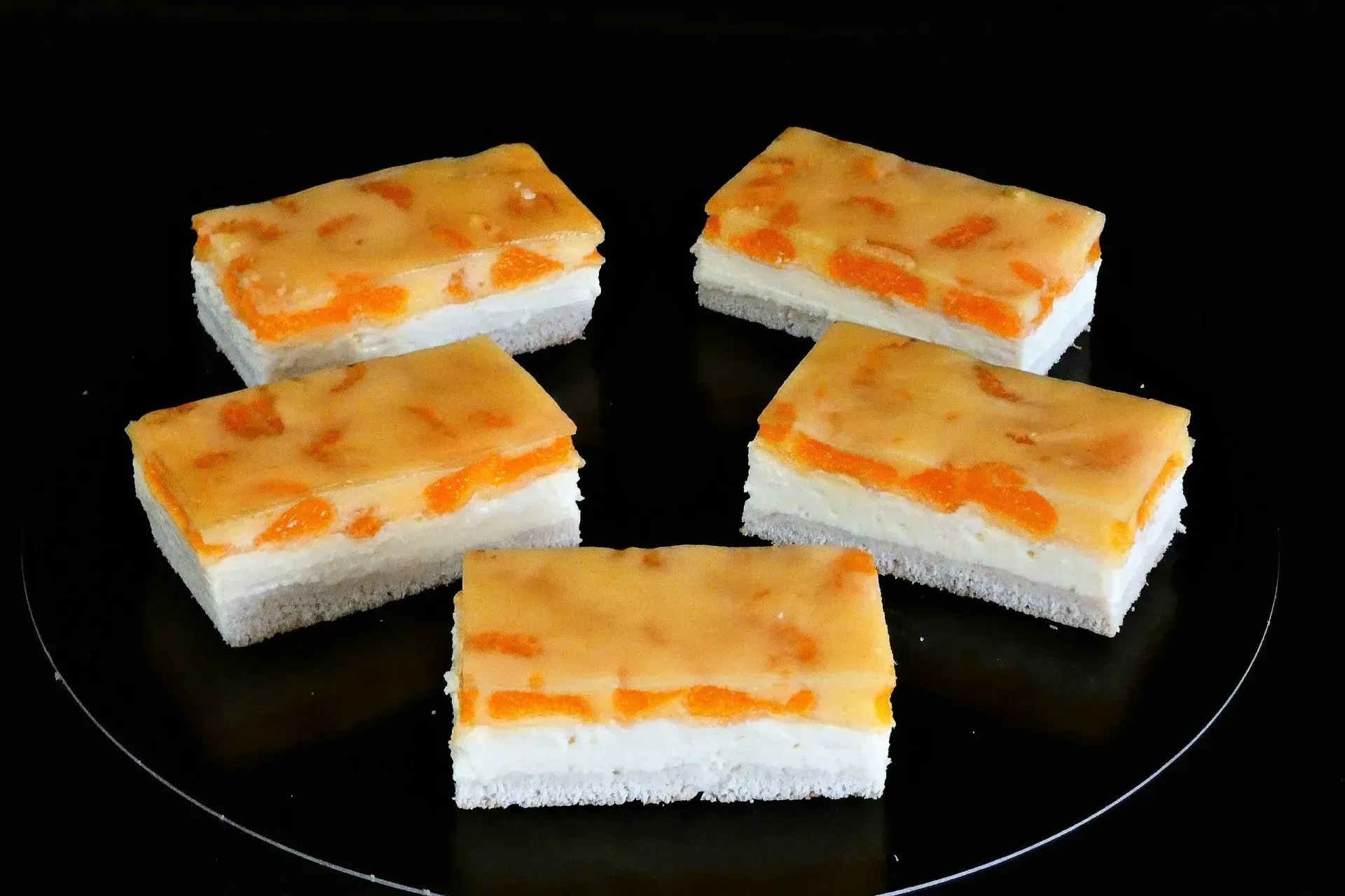 Fünf Stücke eines geschichteten orange-weißen Desserts auf einem schwarzen Teller.