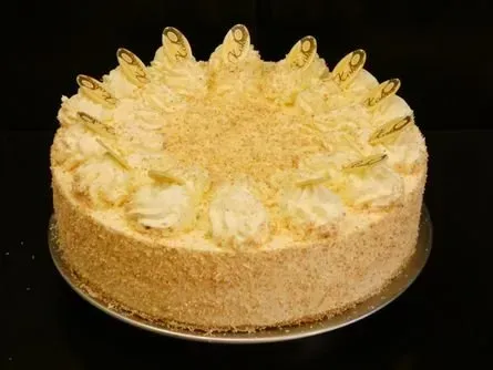 Runder, gelber, glasierter Kuchen mit aufgespritzten Sahnetupfen auf schwarzem Grund