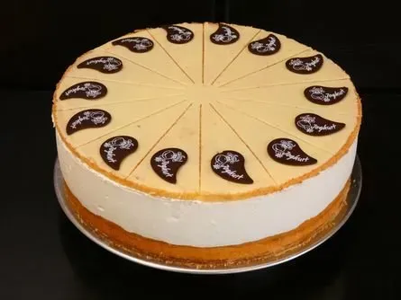 Runder Kuchen mit weißem Zuckerguss und Schokoladendekorationen, auf einer silbernen Platte.