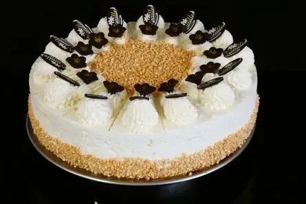 Weißer, glasierter Kuchen mit Schokoladenverzierungen und goldener Streuselfüllung auf schwarzem Hintergrund