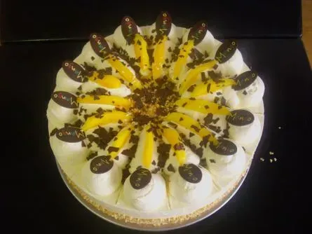 Runder Kuchen mit weißer Sahne, gelbem Zuckerguss und schokoladenüberzogenen Erdbeeren auf schwarzem Hintergrund