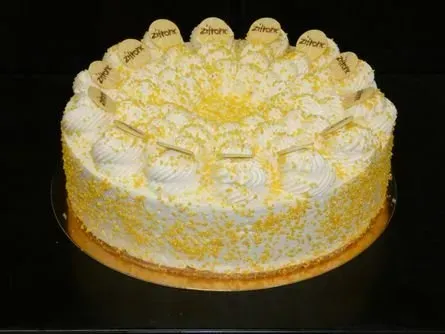 Weißer, glasierter Kuchen mit gelben Streuseln und dekorativen Wirbeln auf einem runden, goldenen Boden