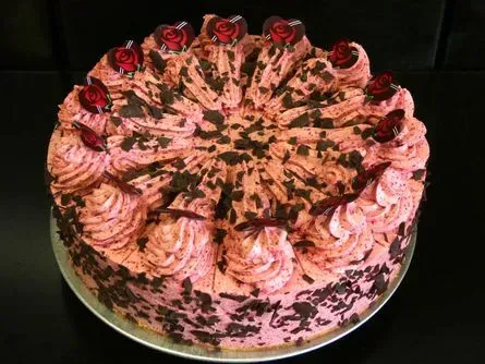 Verzierter runder Kuchen mit rosa Zuckergussrosetten und Schokoladenglasur auf einem Teller