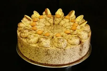 Runder Kuchen mit aufgespritzten Sahnetupfen und goldenen Verzierungen auf einem goldenen Brett