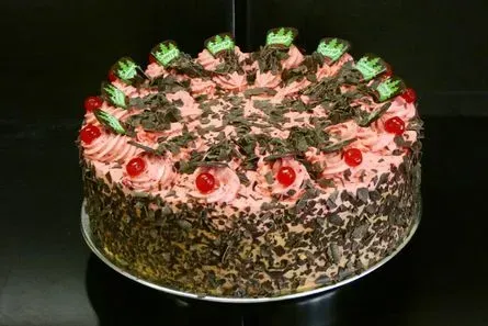 Schokoladenkuchen mit rosa Zuckerguss, Kirschen und grüner Garnierung auf dunklem Hintergrund