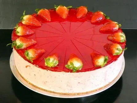 Erdbeer-Käsekuchen auf einem weißen Teller, mit glänzender roter Glasur und Erdbeerscheiben am Rand.