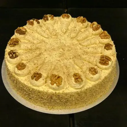 Runder, mit Zuckerguss überzogener Kuchen mit aufgespritzten Rosetten und gehackten Nüssen, vor dunklem Hintergrund.