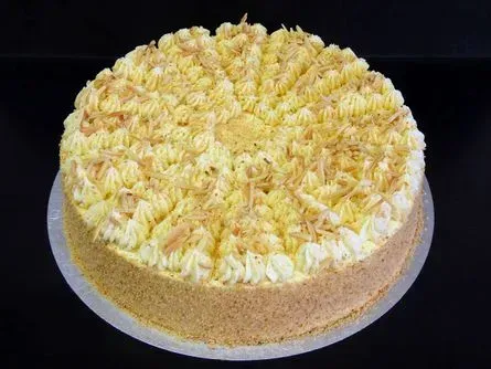 Runder Kuchen mit weiß-gelb gewirbeltem Zuckerguss auf einem silbernen Tablett vor schwarzem Hintergrund