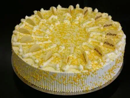 Gelber Zuckergusskuchen mit dekorativen Sahnewirbeln und weißen Schokoladenstückchen auf dunklem Untergrund