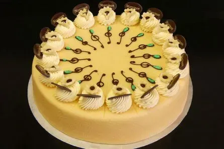 Verzierter runder Kuchen mit muschelförmigen Verzierungen und grünen Akzenten auf einem goldenen Brett