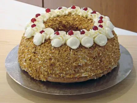 Runder, mit Nüssen bestreuter Kuchen mit weißen Zuckerguss-Tupfen und roten Beeren, auf einem silbernen Tortenbrett